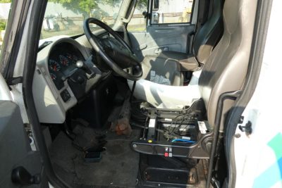 Truck cab interior showing steering wheel and driver's seat of a 2017 International 4300 SBA, with dashboard gauges and a battery/auxiliary box in the cab floor area.
