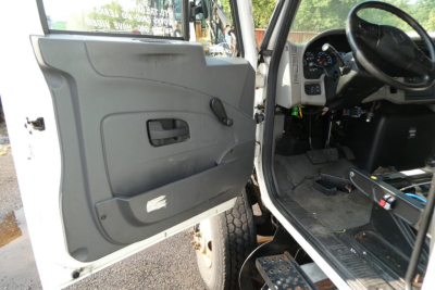 Truck cab interior showing driver’s door panel with window crank, steering wheel, and dashboard visible.