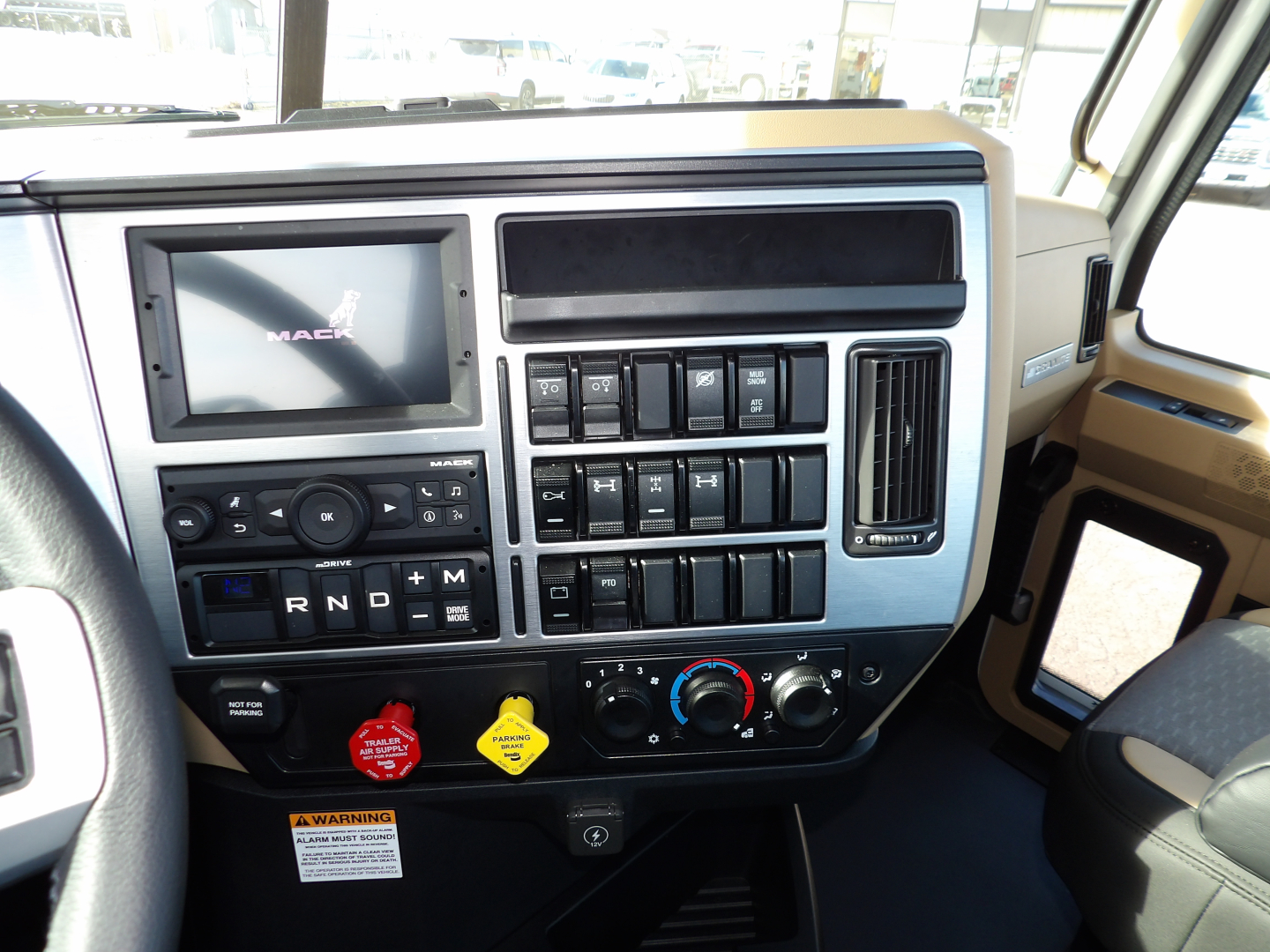 Cab interior of 2025 Mack GR104F showing dashboard with Mack logo on screen, multiple switches, climate controls, and gear selector area.