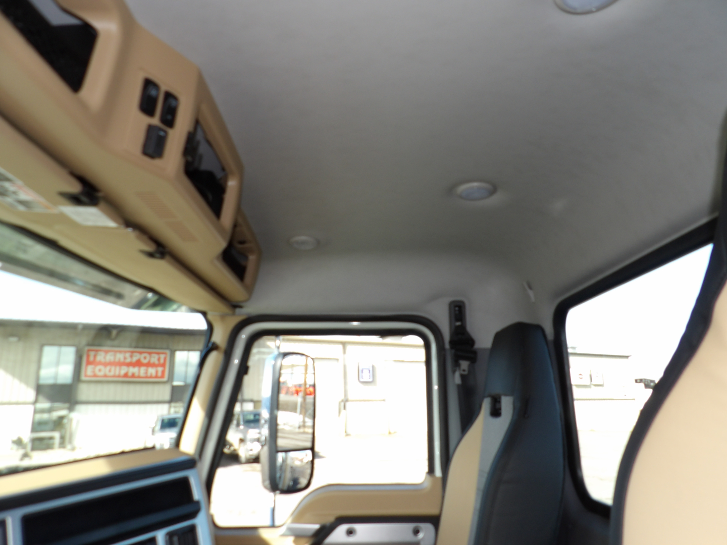 Cab interior of a Mack GR104F dump truck showing tan dashboard, overhead storage, and driver's seat with window view.