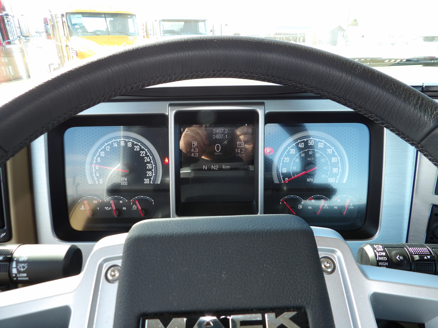 Dashboard and steering wheel view of a Mack GR104F truck cab. Instrument cluster shows speedometer and tachometer flanked by digital display; switches and stalks visible.