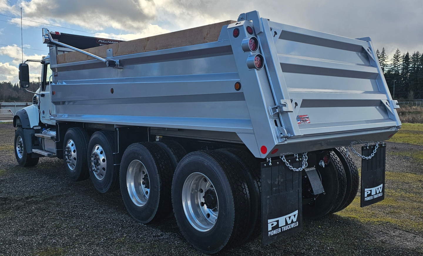 Dump truck rear and side view showing metal dump bed with three-axle setup and rear mud flaps.