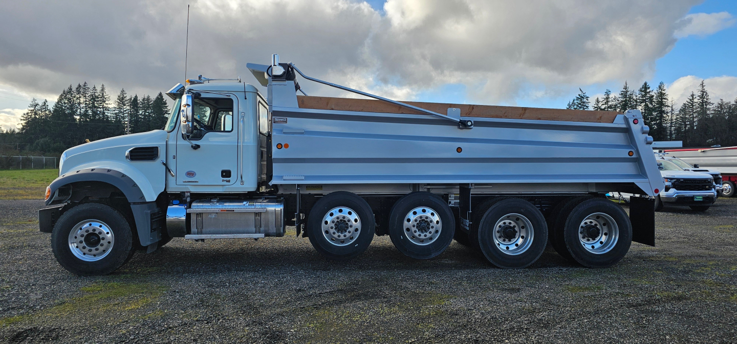Dump truck side view showing Mack GR104F with a large dump body and five rear axles, chrome fuel tank, and California-style cab; no visible text discernible on the truck from this angle.