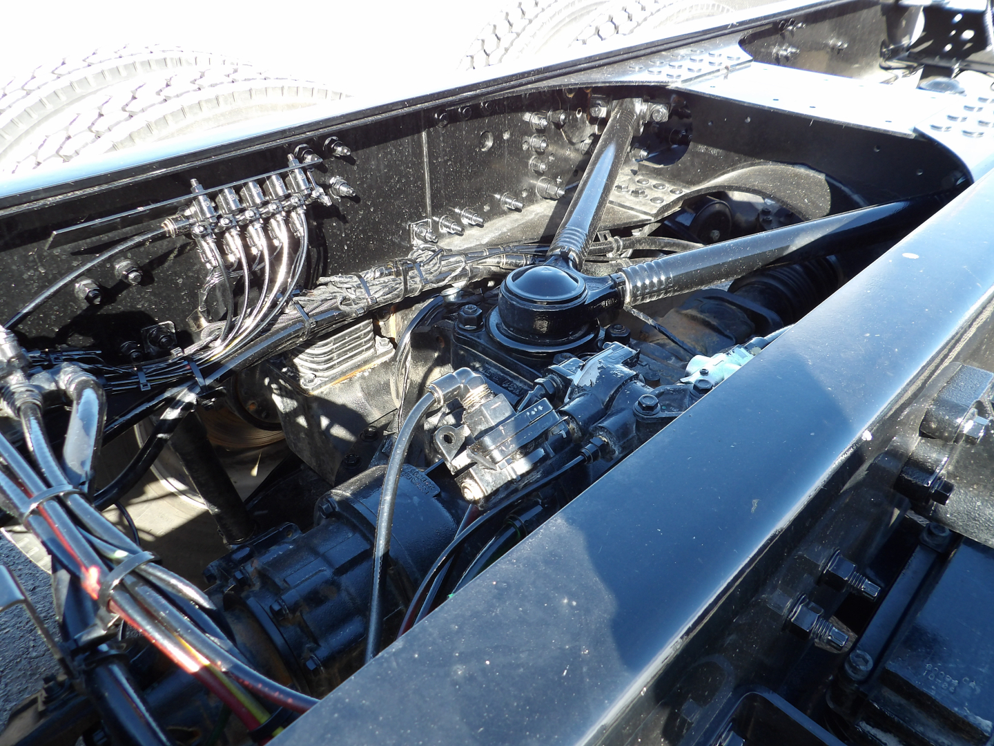 Dump truck engine bay view showing diesel engine with hoses and wiring, Mack GR104F components, hydraulic lines, and chassis frame.