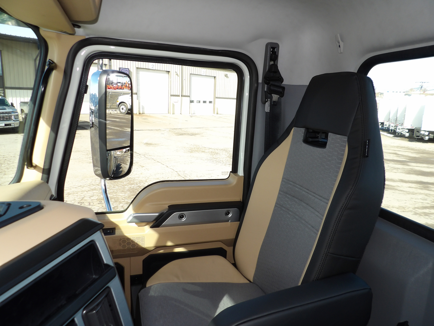 Interior of a 2025 Mack GR104F truck cab showing beige and gray seat, steering area, side mirror, and window frame.