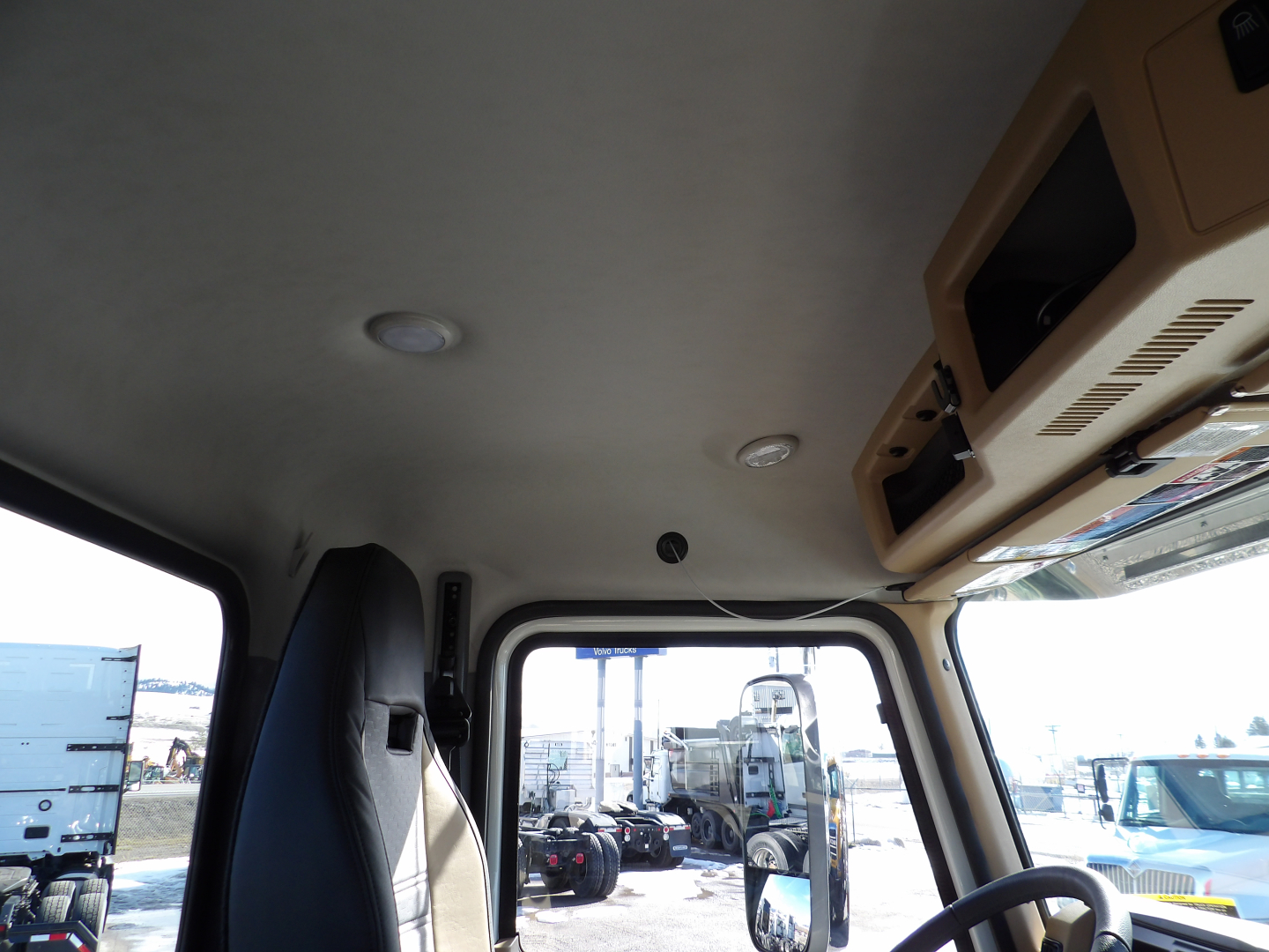 Interior of a new Mack GR104F dump truck cab showing overhead storage compartments and windshield view, with other trucks visible outside.