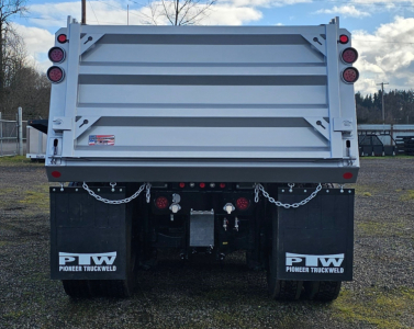 Dump truck rear showing tailgate and dual mud flaps with Pioneer Truckweld logos, taillights, safety chains, and rear bumper.