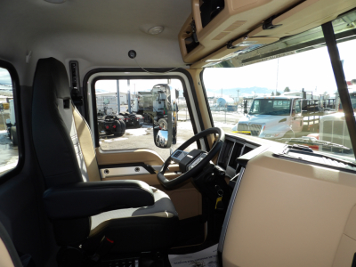 Cab interior of a new 2025 Mack GR104F dump truck showing steering wheel, driver's seat, dashboard, and window with outside equipment.