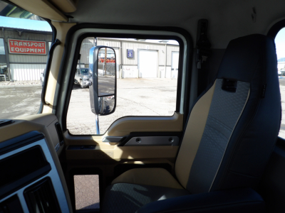 Truck cab interior with steering wheel, passenger seat, and window view; side mirror and exterior lot visible.