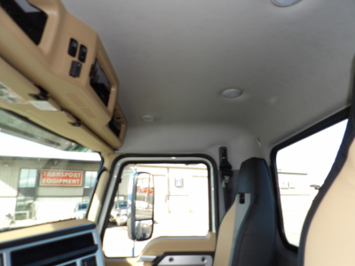 Cab interior of a Mack GR104F dump truck showing tan dashboard, overhead storage, and driver's seat with window view.