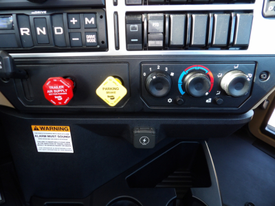 Dashboard view of a 2025 Mack GR104F truck showing RND shift panel, two colored knobs (red trailer air supply and yellow parking brake) and climate controls.