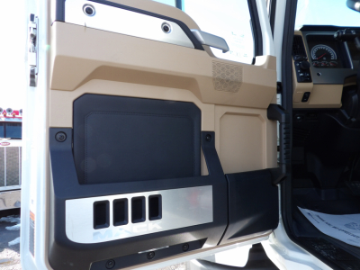 Truck door panel interior of a 2025 Mack GR104F dump truck showing beige plastic and black storage pocket with metal accent; part of dashboard and steering wheel visible.