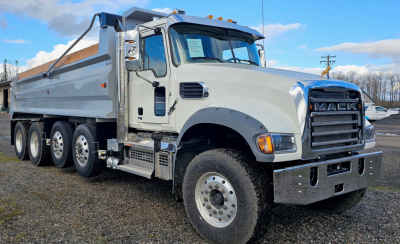 Dump truck showing Mack GR104F front grille and multiple axles, light gray cab, white dump bed, stock number 68645 visible.