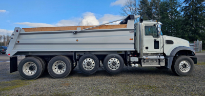 Mack GR104F dump truck side profile showing silver dump body, white cab, six wheels, chrome steps, and VIN/stock details not visible on image.