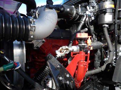 Truck engine bay with red engine block, intercooler piping, hoses, and battery area visible; shows components and wiring but no legible serials on this view.