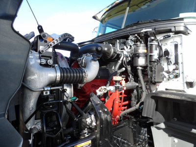 Engine bay of 2025 Mack GR104F dump truck showing engine block, hoses, and components with red engine parts and black intake piping.