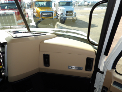 Truck cab interior of a 2025 Mack GR104F showing steering area and dashboard with tan panels and a Mack badge.