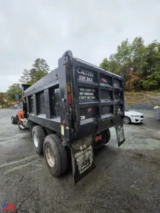 Dump truck rear view showing steel dump bed with caution decals and mud flaps. Text on bed reads CAUTION STAY BACK YOU CAN'T SEE MY MIRRORS CAN'T SEE YOU.