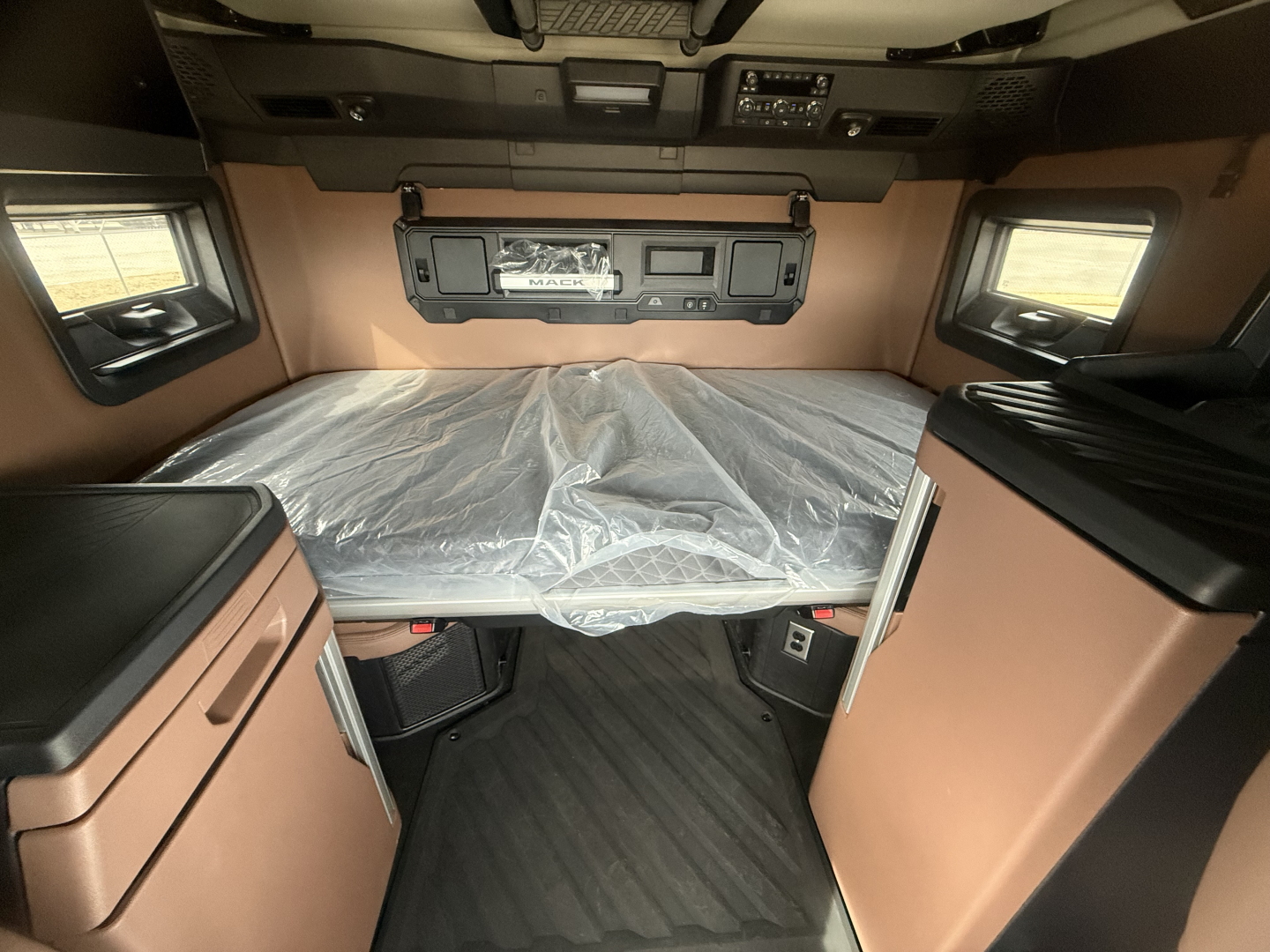 Mack PR64T76H cabin interior with bed platform covered in plastic, overhead control panel, and storage cabinets on both sides.