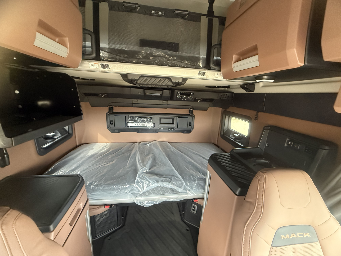 Interior sleeper cab of a 2026 Mack PR64T76H showing bunk, overhead storage, and control panel with tan upholstery.