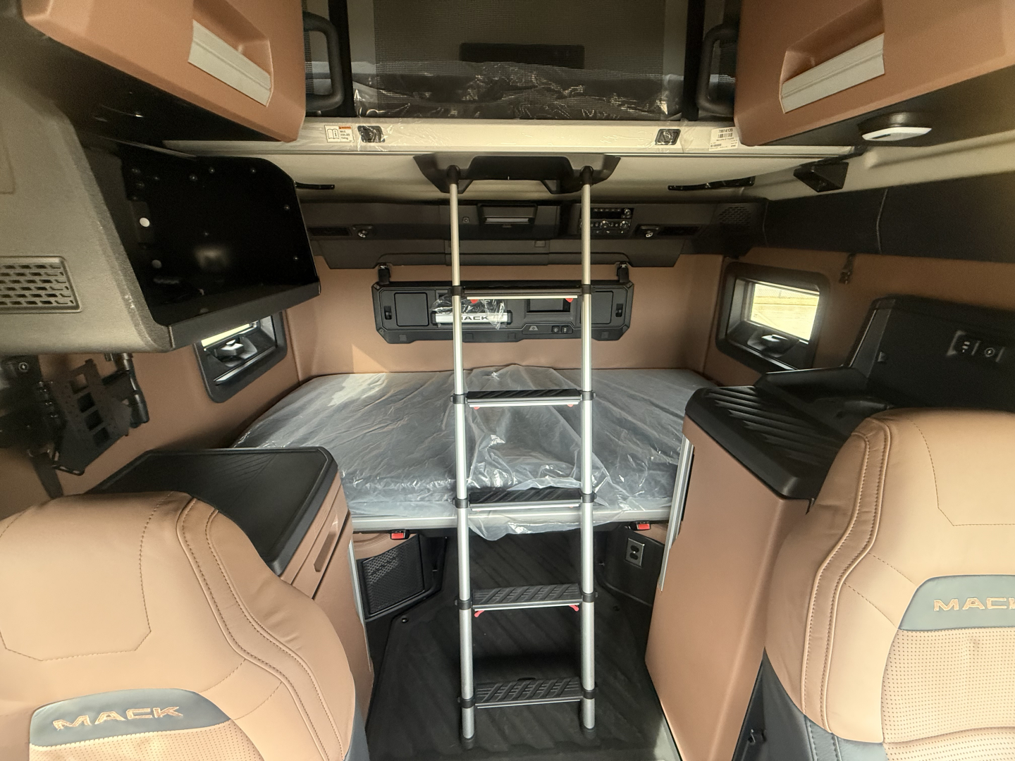 Mack PR64T76H sleeper cab interior showing bunk bed area with ladder and tan leather seats.