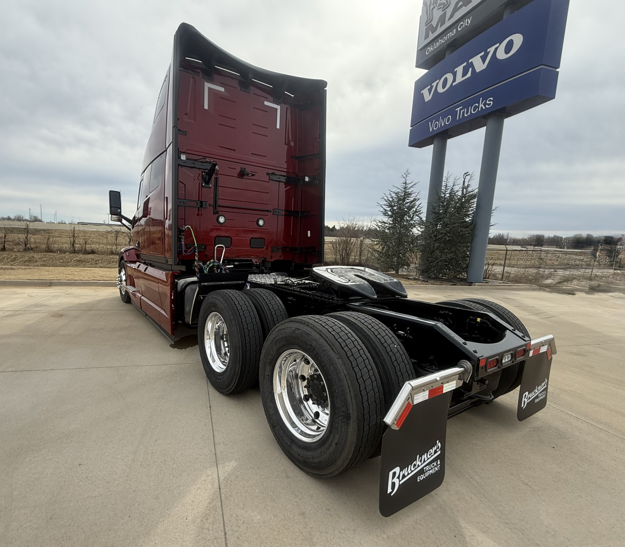 Truck chassis back and cab of a new Mack PR64T76H conventional sleeper. Visible text includes Volvo sign and Bratman? Mudflaps say Mack Trucks? License plate area not legible.