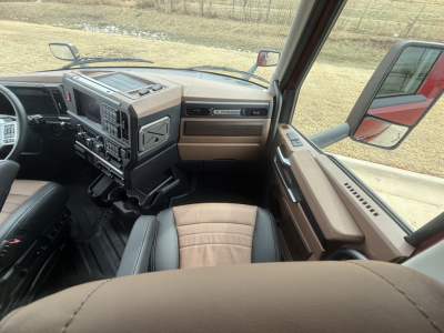 Truck cabin interior with steering wheel to left, dashboard and center console, tan and black seats, Mack PR64T76H cab views.