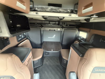 Cab interior of a new 2026 Mack PR64T76H sleeper with brown and black leather seats, overhead bunk area, center table, and compact dashboard.