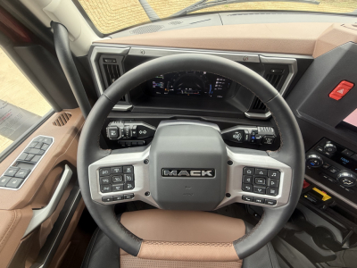 Mack PR64T76H truck interior showing steering wheel with multifunction controls, digital gauge cluster, brown leather trim, and dash panels.