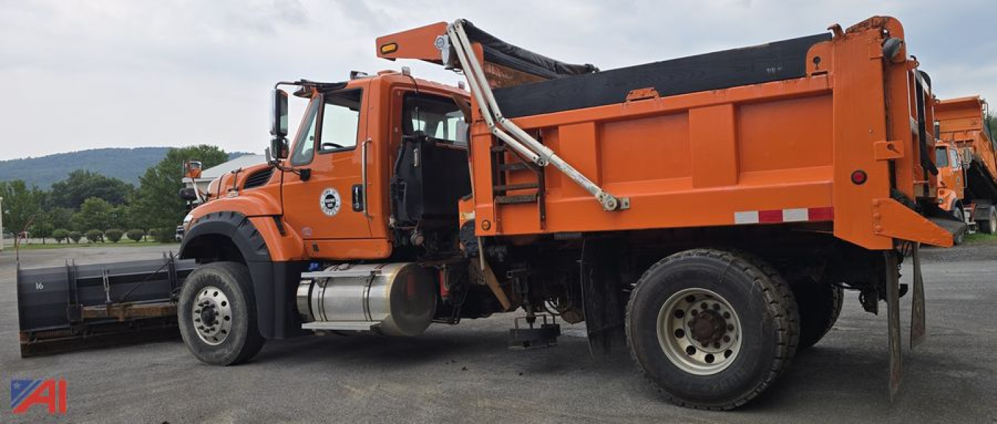 Dump truck with plow and hopper shown side view. 2018 International 7600 SFA dump truck in orange with plow attachment and side-mounted fuel tanks.