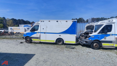 Ambulance body with blue and white livery, side view showing storage compartments and rear; ambulance truck in lot with others in background.