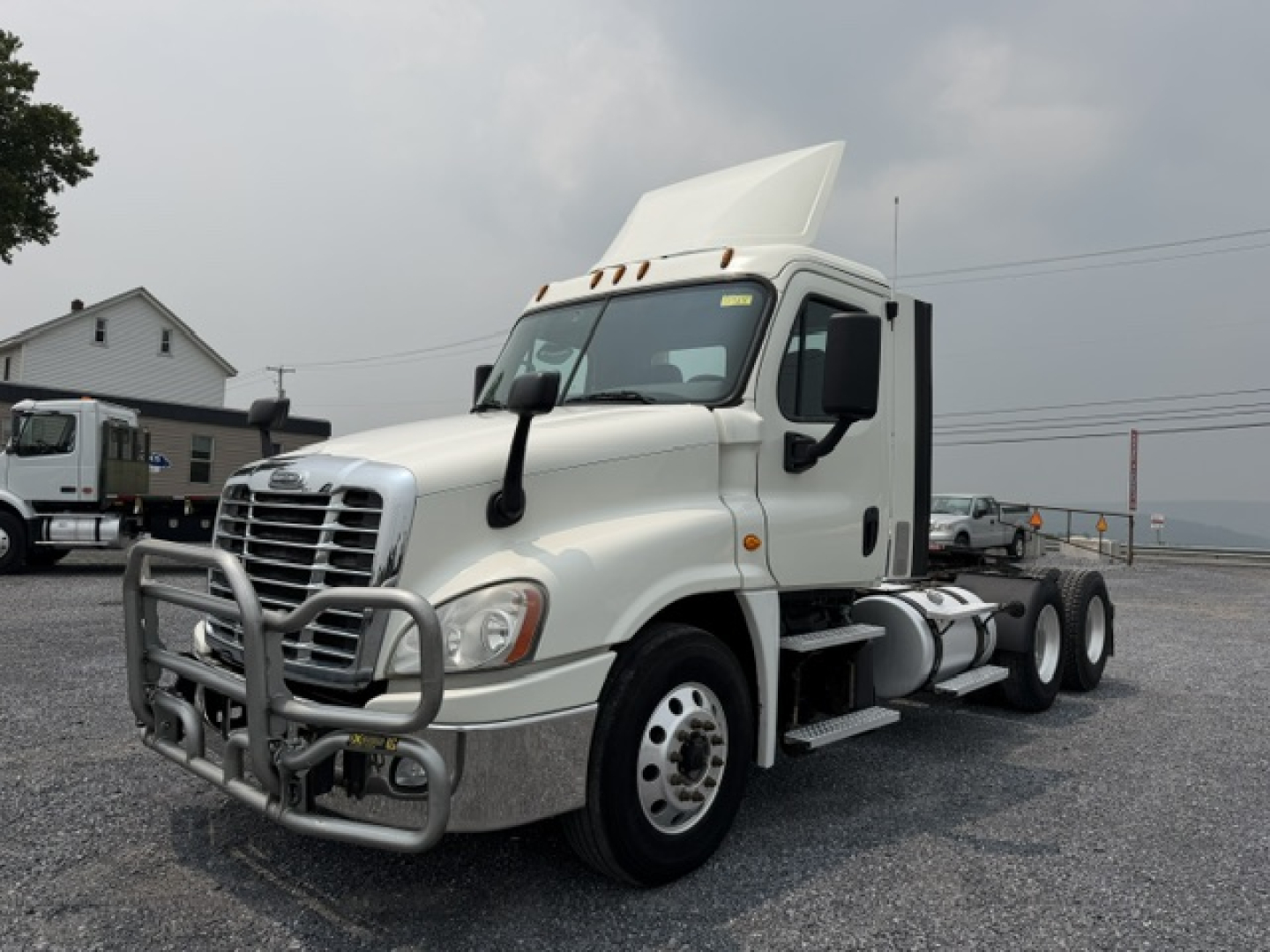 Truck cab and trailer chassis of a white 2017 Freightliner Cascadia CA125DC with a raised hood and front bumper guard.