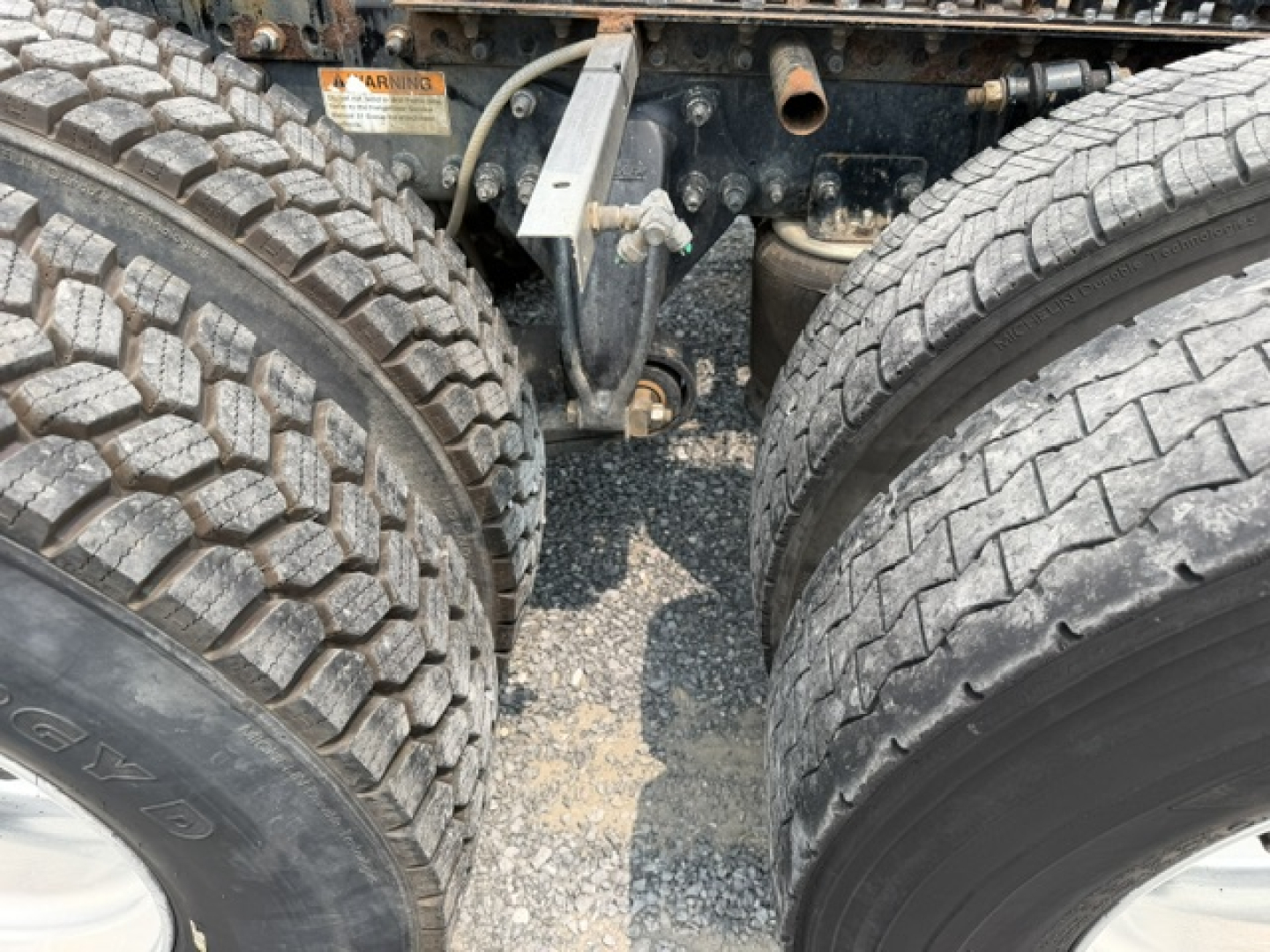 Truck chassis shown between dual rear axles with rugged tires and suspension components visible.