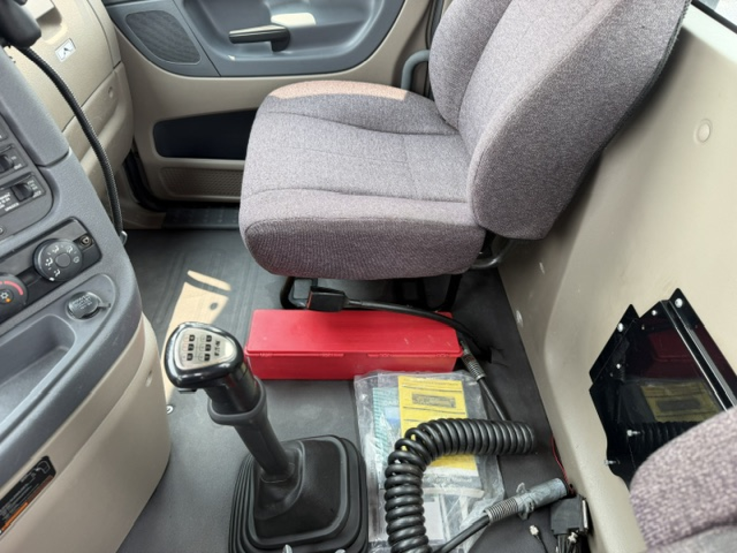 Cab interior of a 2017 Freightliner Cascadia CA125DC with a manual shifter, driver seat, and red battery jump pack visible near the floor along with coiled cable.