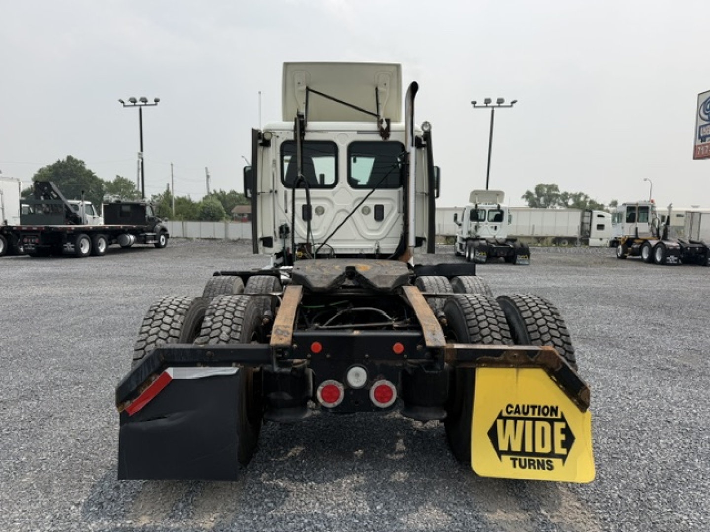 Rear view of 2017 Freightliner Cascadia CA125DC tractor chassis showing dual rear axles, mud flaps, and ‘Caution Wide Turns’ sign.
