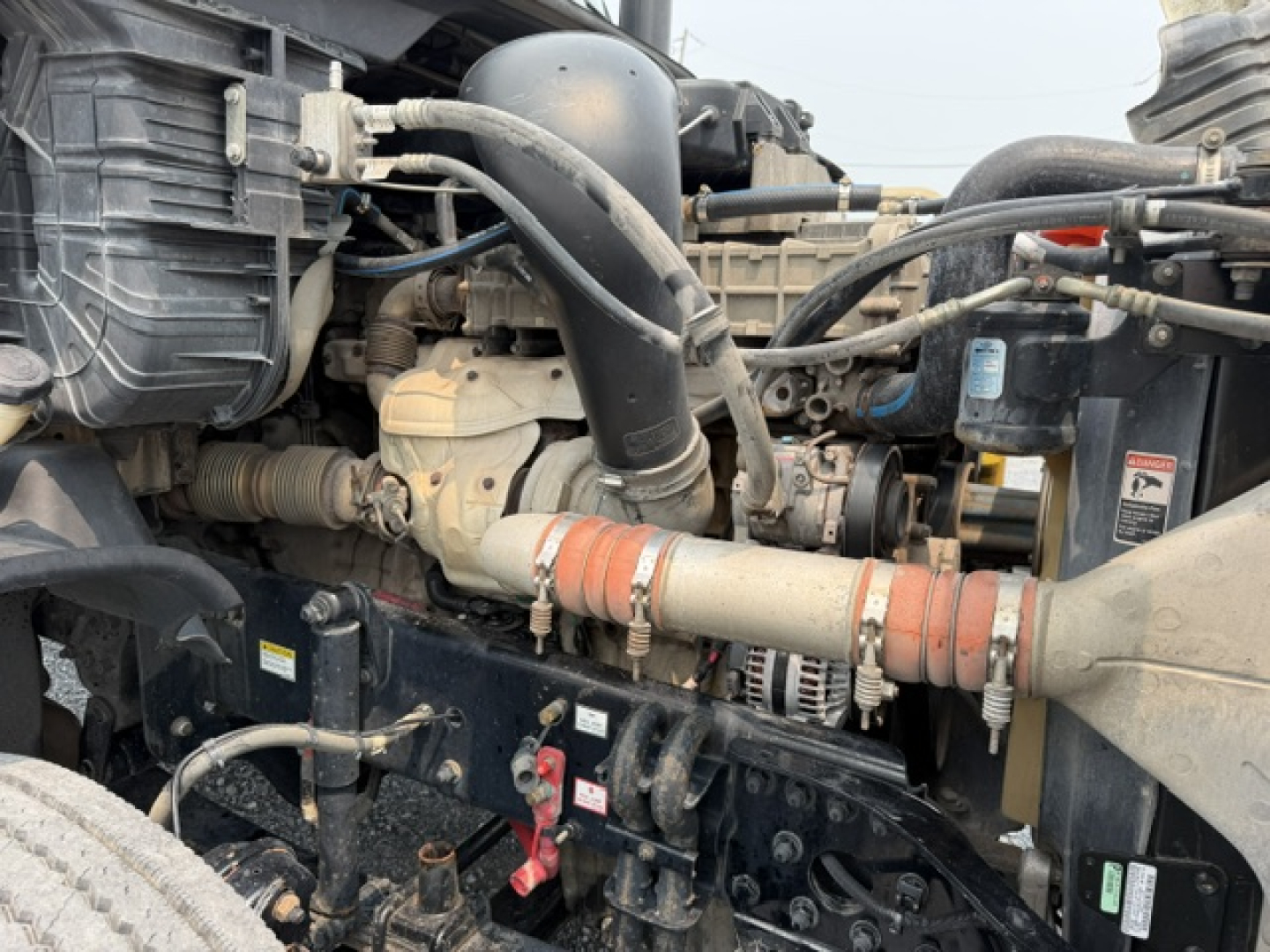Truck engine bay showing intake manifold, hoses, and coolant/radiator lines in a Freightliner Cascadia engine bay.
