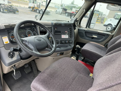 Freightliner Cascadia driver’s cab interior showing steering wheel, instrument cluster, and dashboard controls in a daycab truck.
