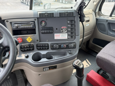 Cab interior of a 2017 Freightliner Cascadia CA125DC showing dashboard controls, steering wheel, gear selector, radio, air vents, cup holders, and passenger seat.