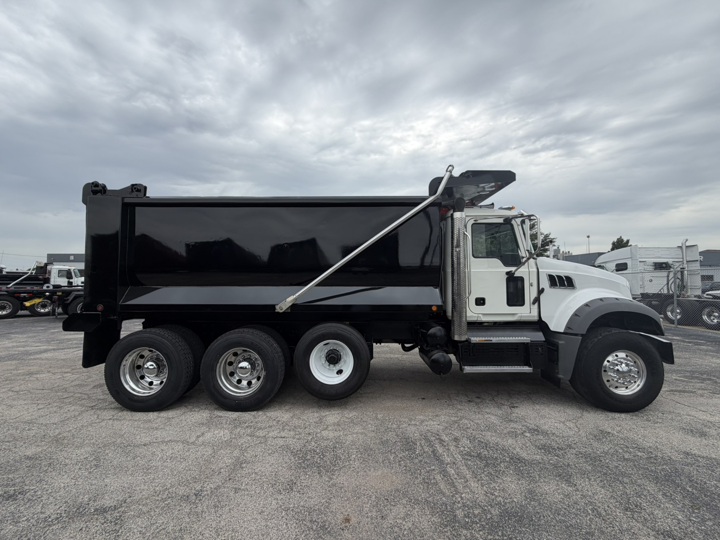2021 Mack GR64F dump truck side view showing black dump body, white cab, wheels, and hydraulic dump mechanism.