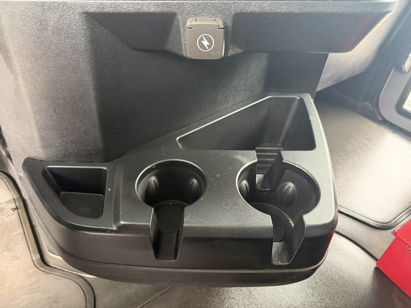 Truck interior storage area with cup holders and a front armrest in the cab.
