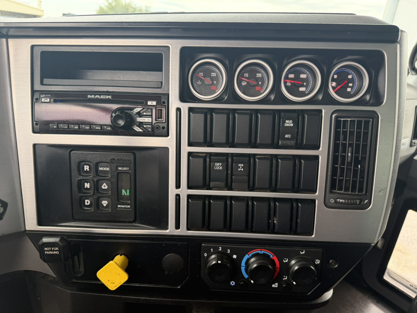Dashboard panel of a 2021 Mack GR64F dump truck showing gauges, radio, climate controls, and gear selector area with yellow key tag.