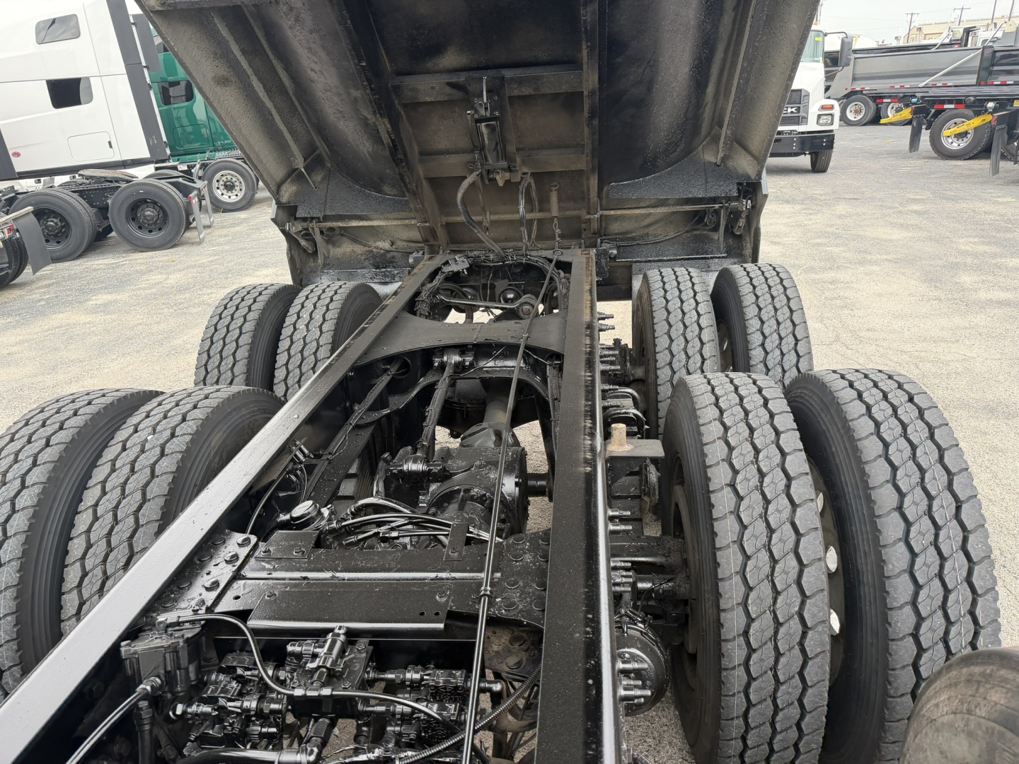 Truck chassis under dump bed showing drivetrain and rear axles with dual tandem setup.
