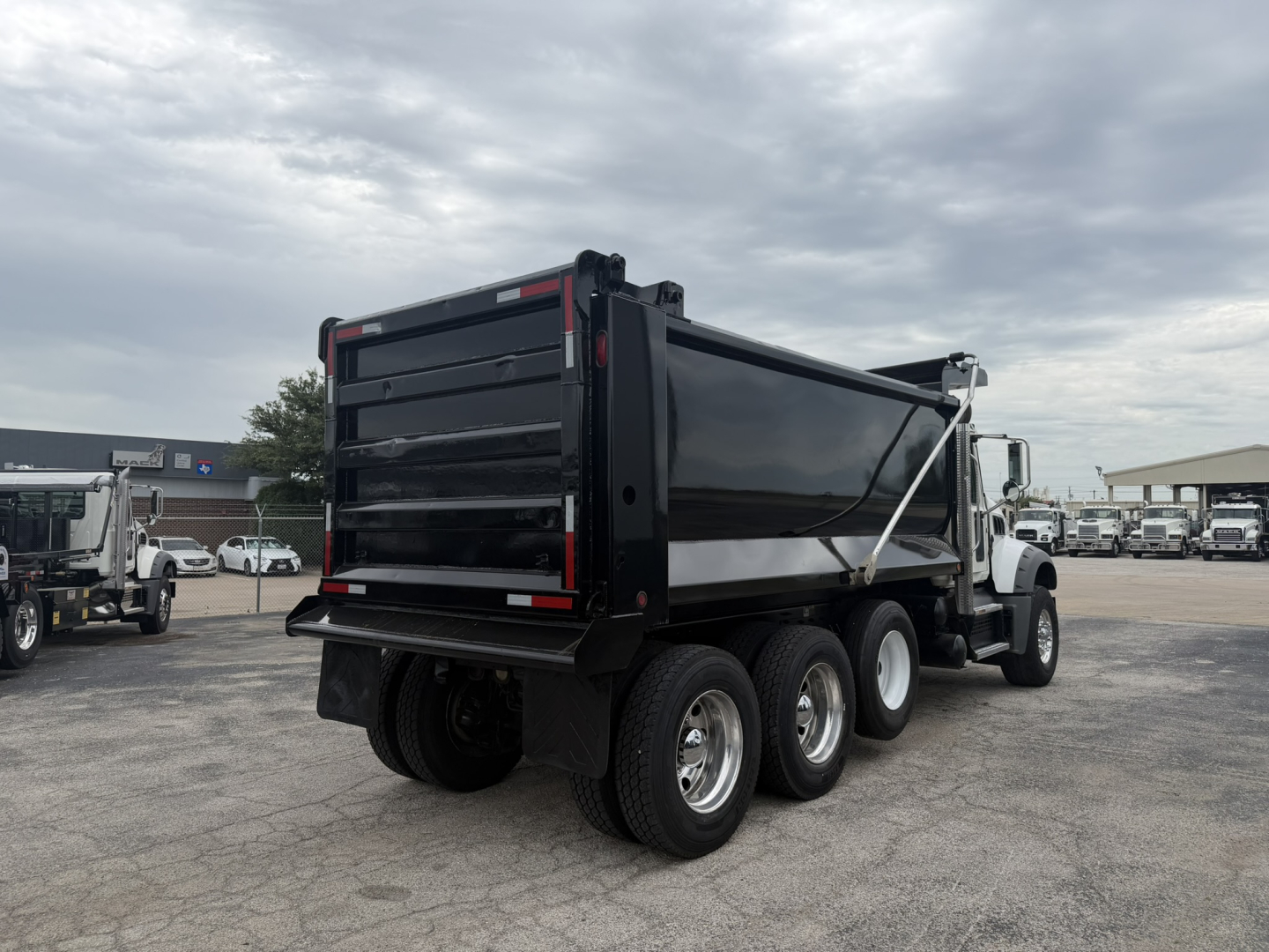 Dump truck rear and side view showing three-axle Mack GR64F dump bed with black bed and white cab, drivetrain and wheel setup visible.