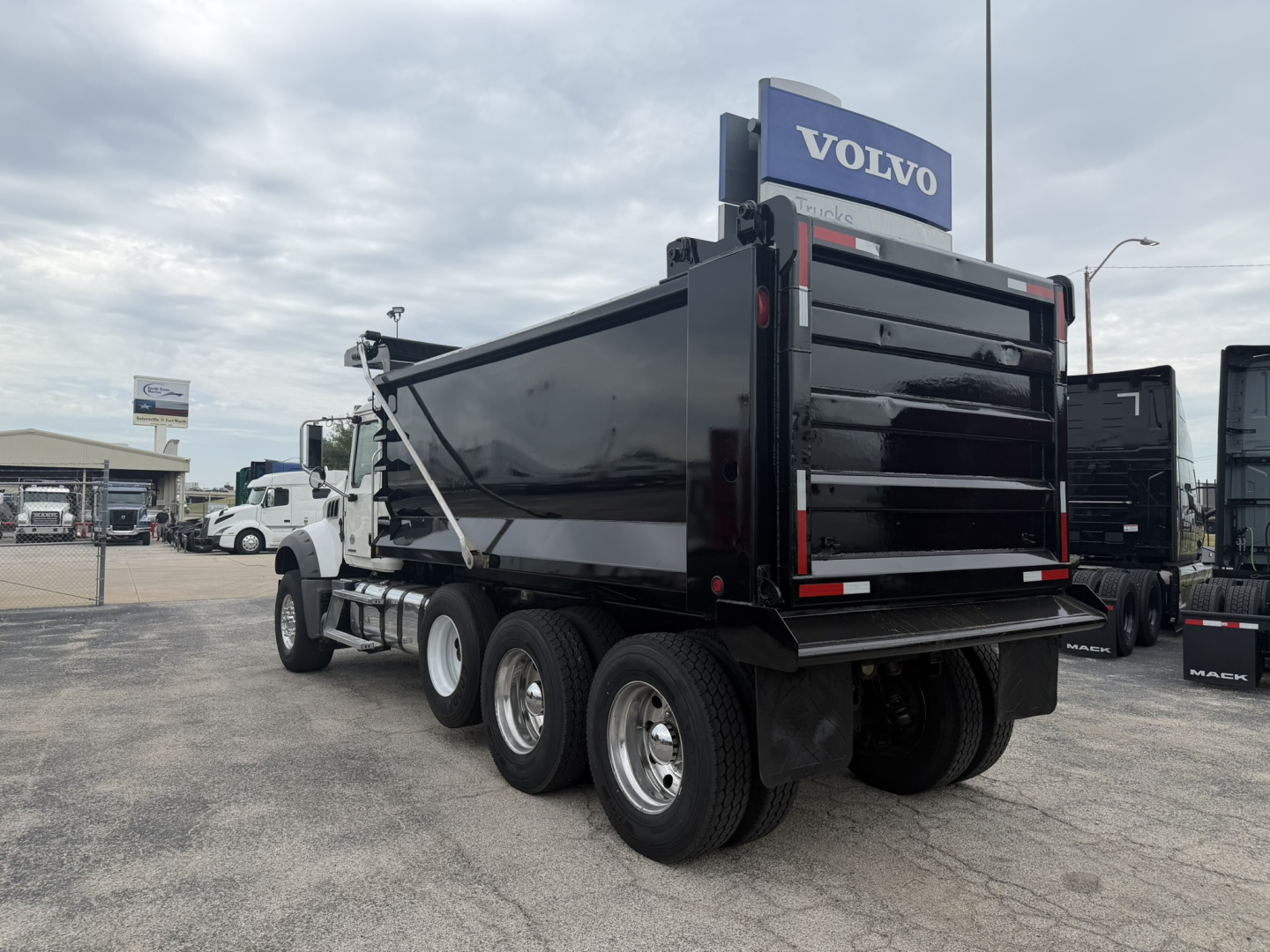 Mack GR64F dump truck rear view showing black dump bed and Volvo dealership sign
