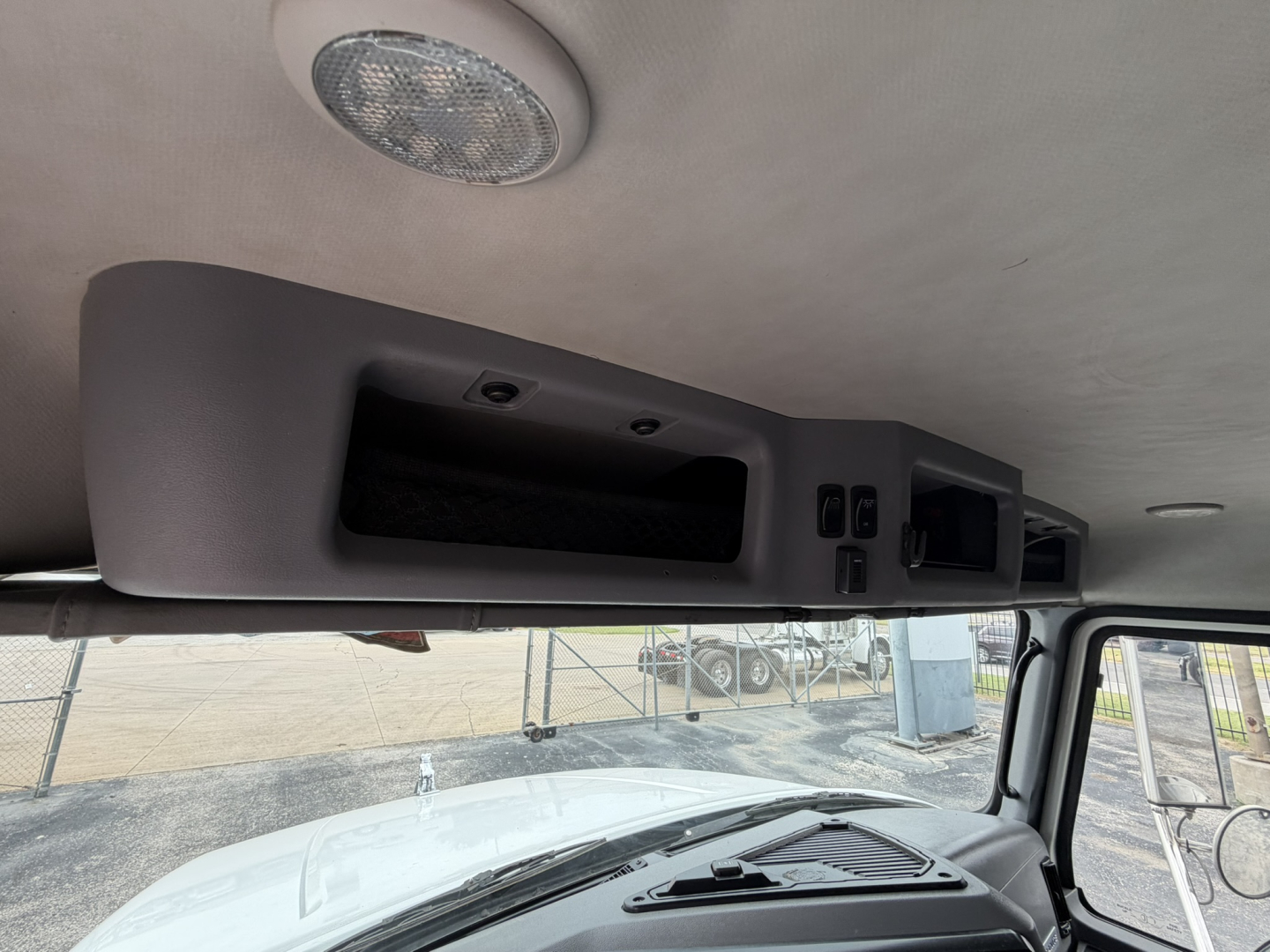 Dump truck cab interior showing overhead console with small compartments and controls, windshield, and ceiling-mounted dome light.