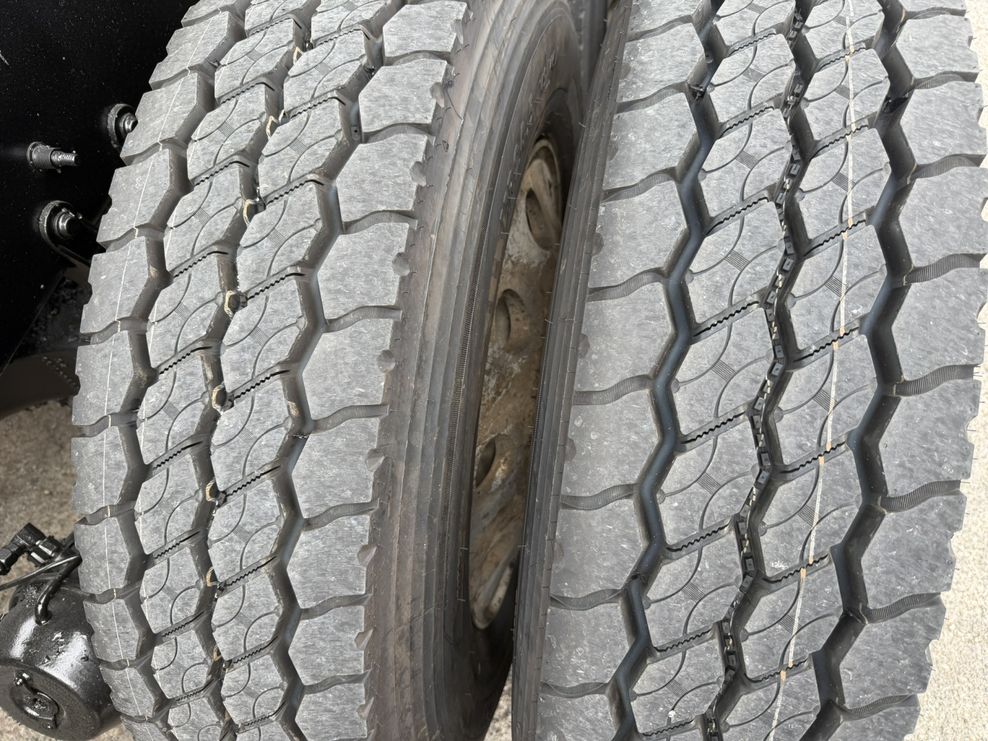 Mack GR64F truck wheel and tire close-up showing dual rear wheels and tread pattern.