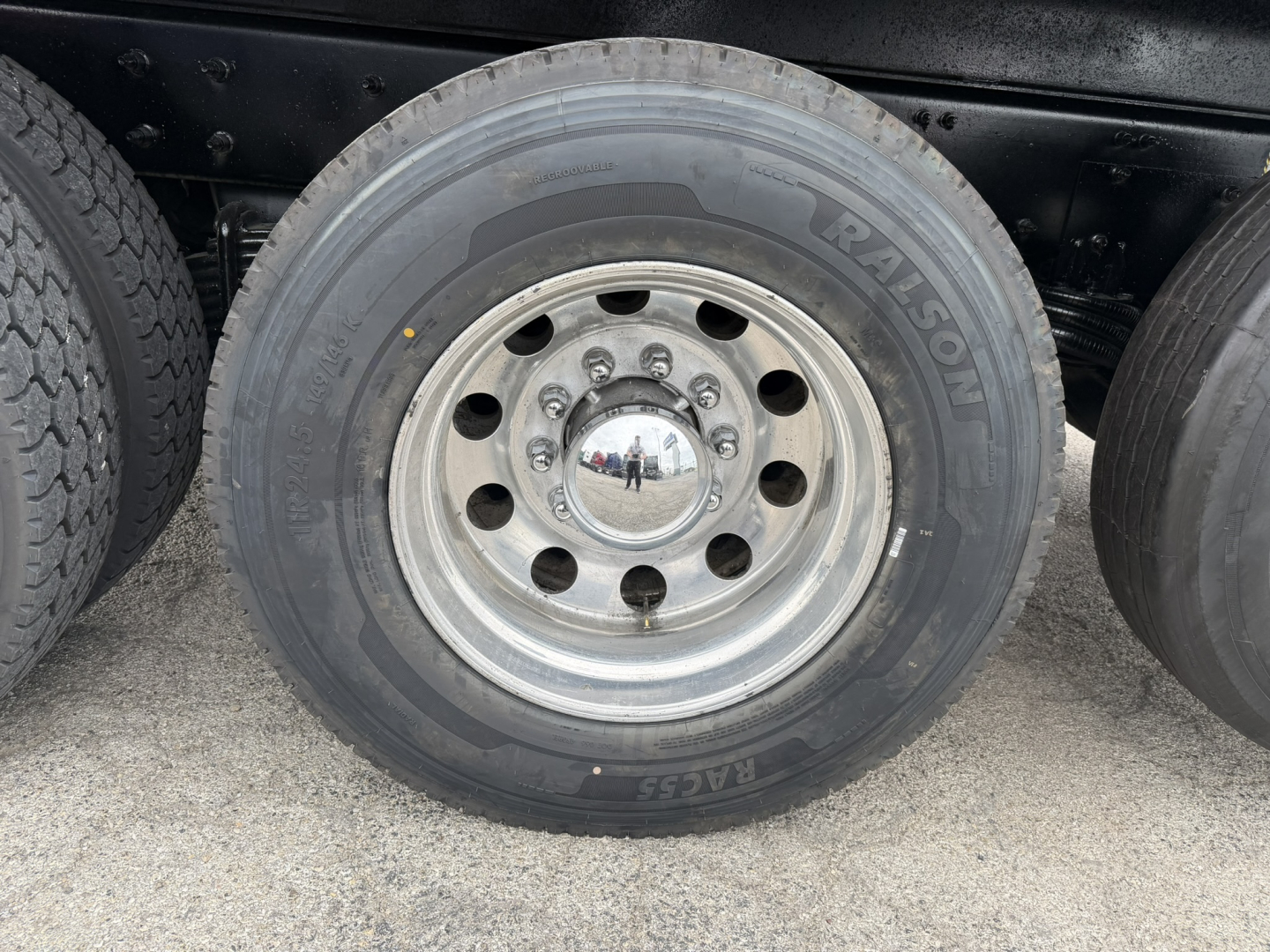Wheel and tire on Mack GR64F truck showing coil spring hub and RALISON?? brand On tire sidewall with text 'TALISON' or 'RAISON'? The visible text includes 'RAISON' and 'EAGLE' maybe. chrome center cap reflection. Rim with multiple lug nuts.
