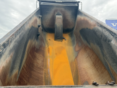 Dump truck bed interior with orange chute and black sides, showing worn bed liner and side rails in a Mack GR64F with loading area open.
