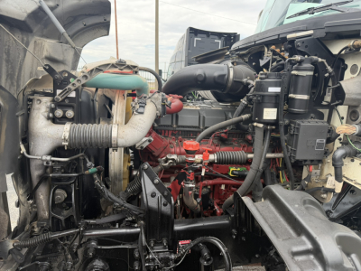 Tractor-trailer truck engine bay showing red engine block, hoses, and components with air intake and hoses visible.