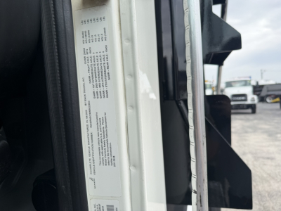 Tag sticker on Mack GR64F door jamb with vehicle specifications and VIN. Visible text includes numbers and warning label in a narrow column on the door hinge area.